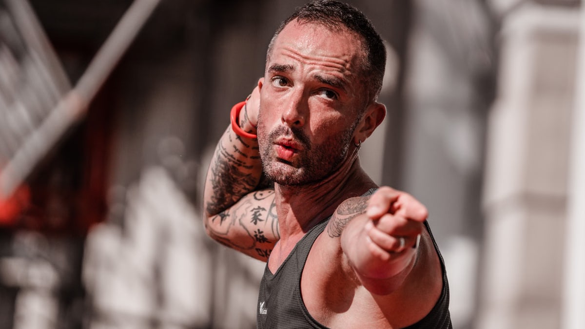 Tattooed man in a tank top points with focus during outdoor fitness activity in A Coruña.